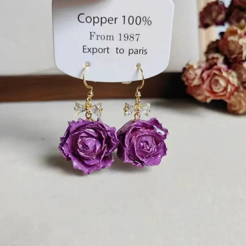 Elegant Immortal Rose Long Earrings with purple epoxy roses, gold hooks and crystal bow accents by Simples Market