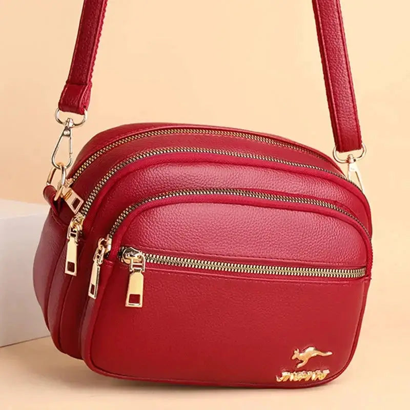 Red soft leather purse with multiple gold-zip compartments and a shoulder strap, front pocket.