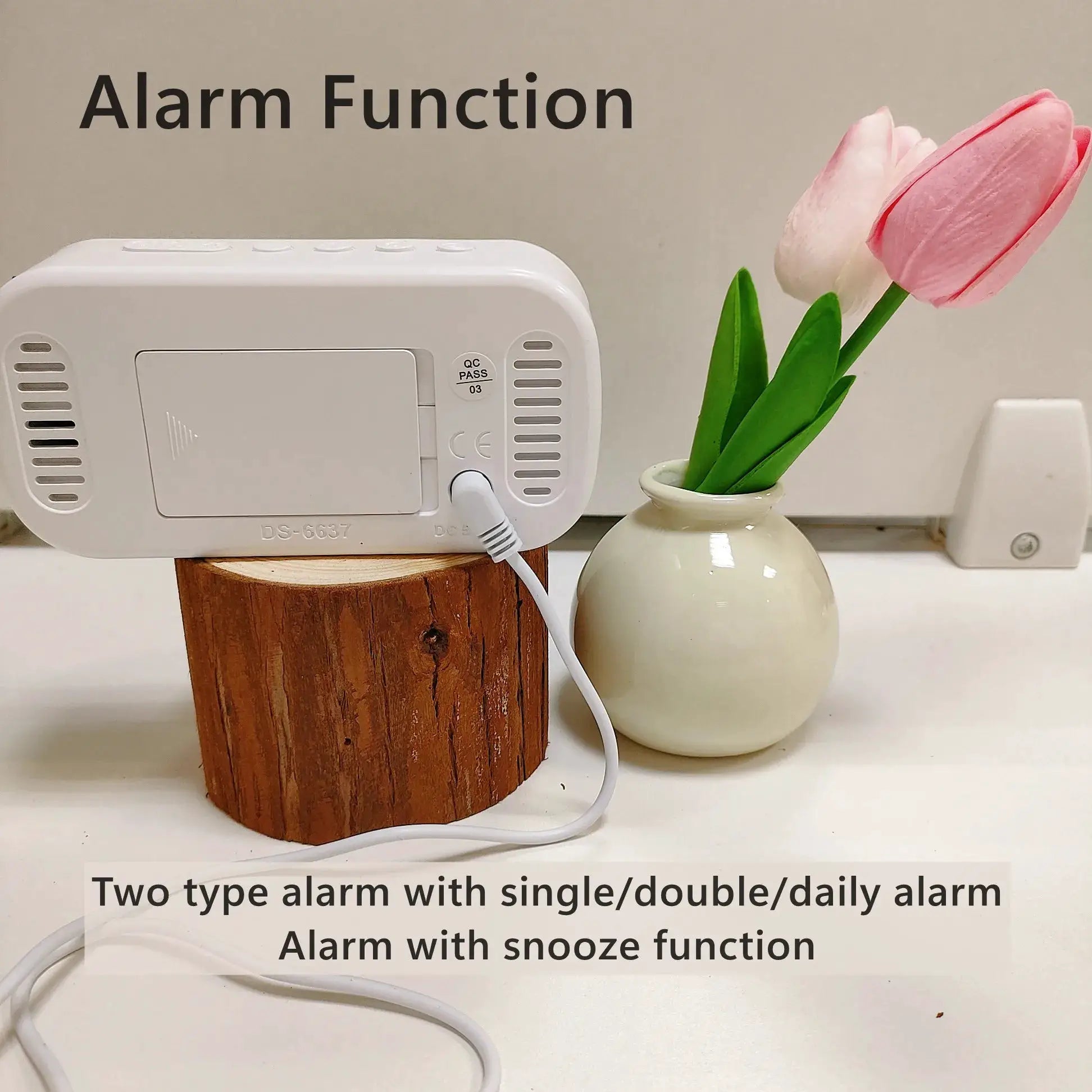 White USB-powered digital alarm clock on a wooden block beside a pink tulip vase