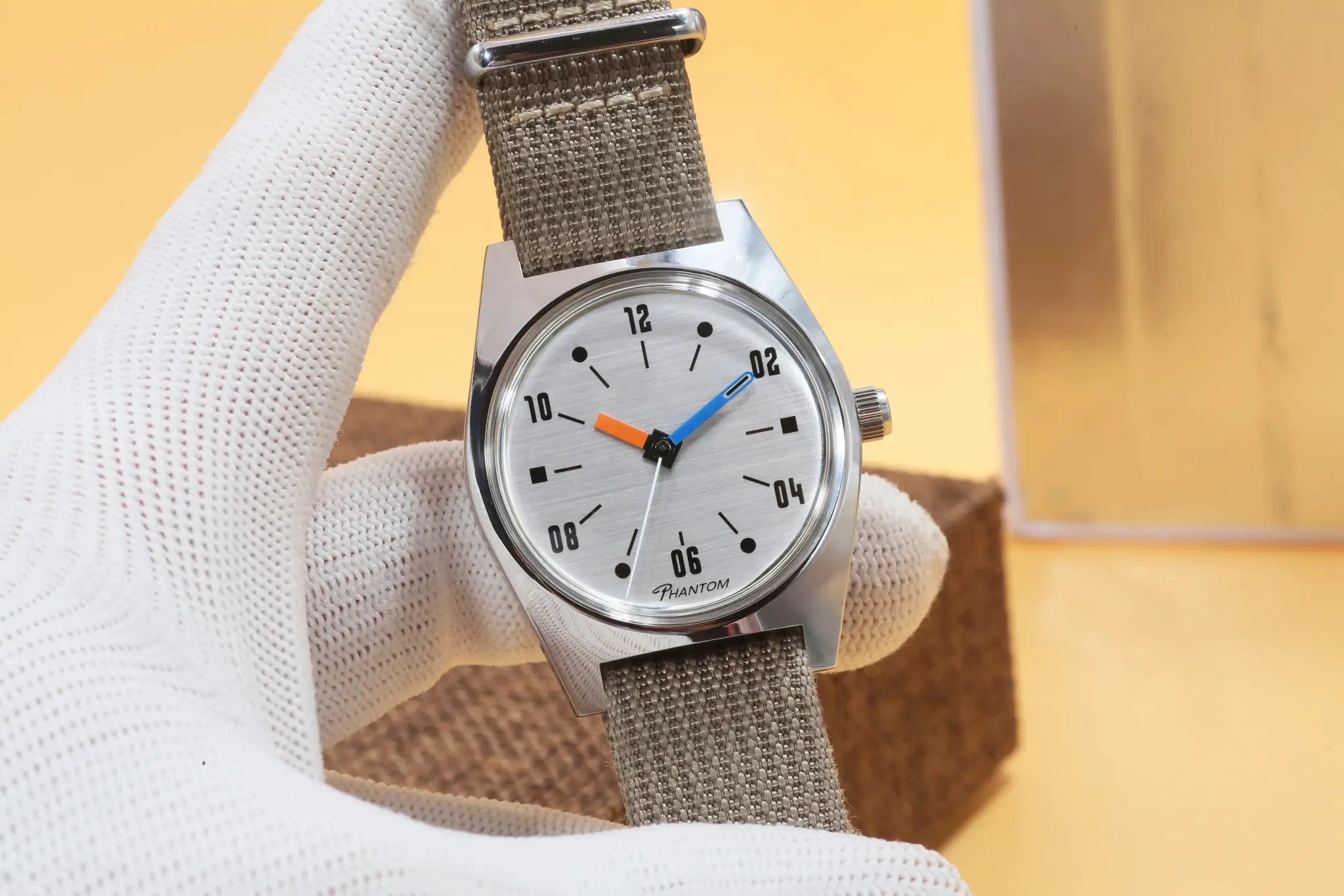 7120 hand-wind mechanical watch by Simples Market; 36mm silver dial with blue and orange hands and olive fabric strap.