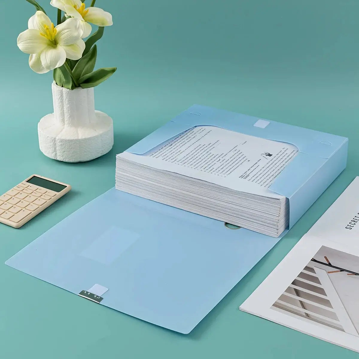 Large blue foldable plastic file box with thick A4 document stack on teal desk.