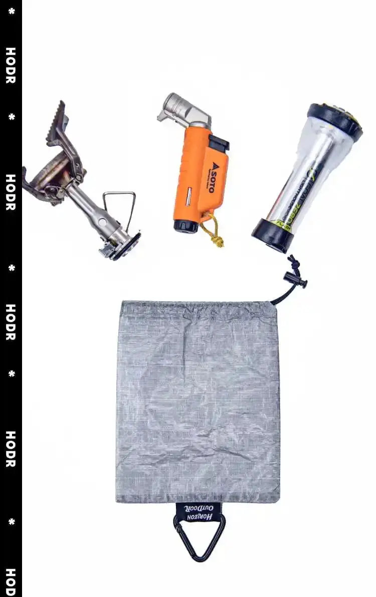 Stashlite Dyneema DCF stuff sack by Simples Market; gray cuben-fiber bag with drawcord and carabiner, shown with ultralight camping gear.