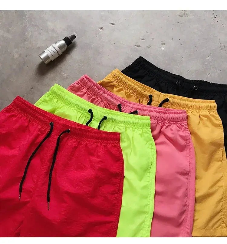 Men's swim shorts in a six-color assortment with black drawstrings, laid out for display.