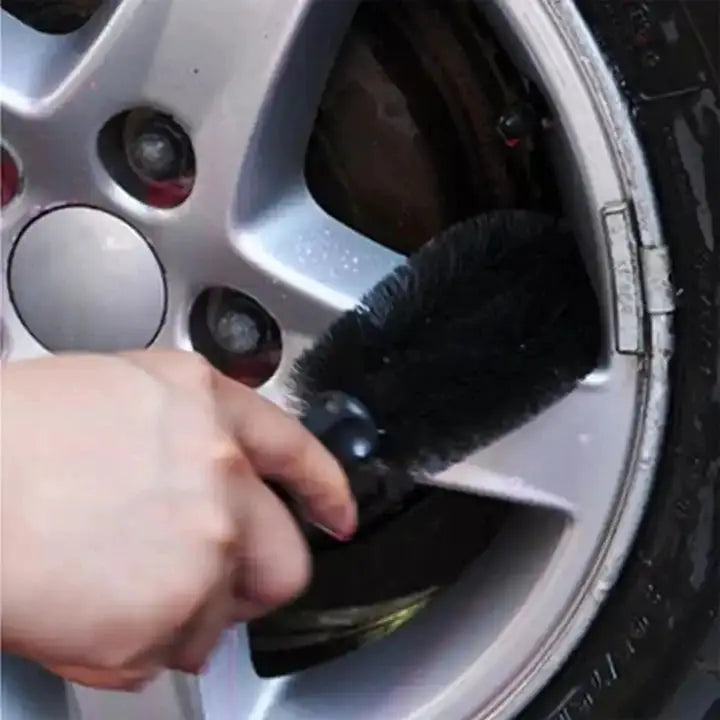 Car wheel cleaning brush with black bristles cleaning a silver alloy rim.