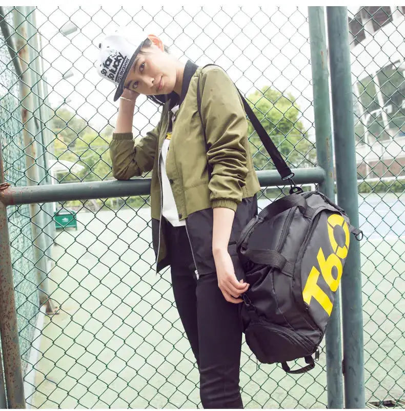 Gym bag backpack, black waterproof fabric with bold yellow lettering, carried by a woman in a green jacket.