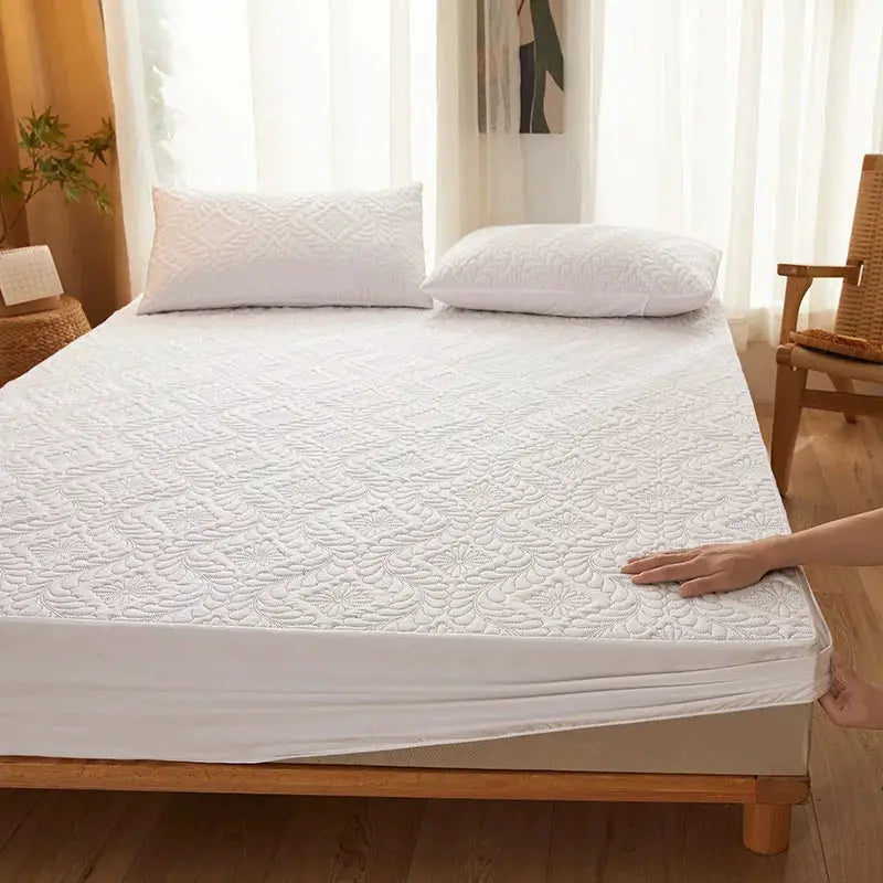 Waterproof quilted mattress protector, white, fitted on a bed with two matching pillows.