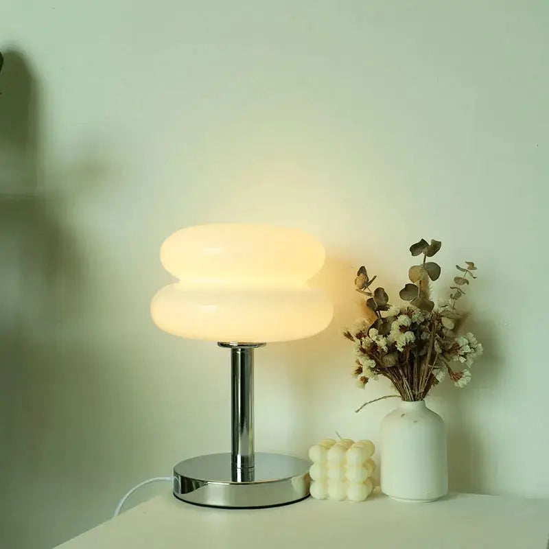 Macaron glass table lamp with chrome base and warm glow; bedside decor beside a dried flower vase