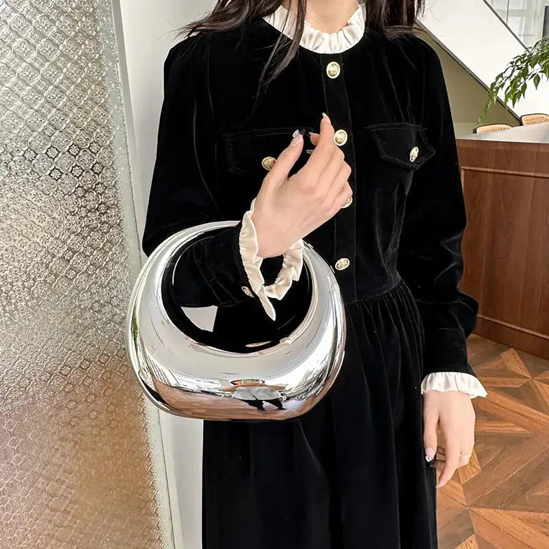 MOODS silver round-handle evening handbag by Simples Market, carried by a woman in a black velvet dress