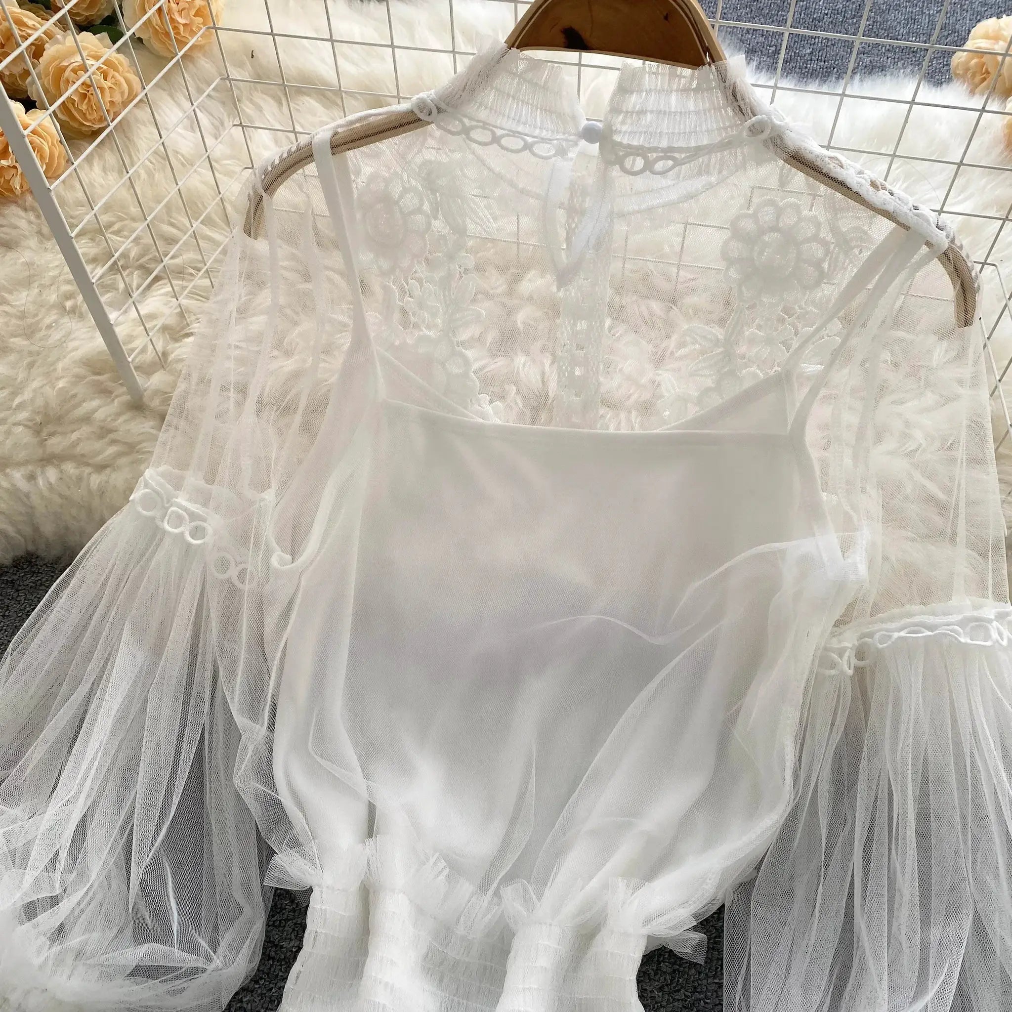 White lace puff-sleeve blouse on a hanger; sheer floral lace with high neck.