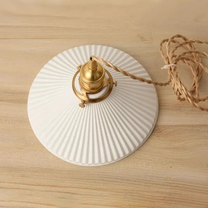 Round white ribbed ceramic pendant light with brass hardware and natural jute cord.
