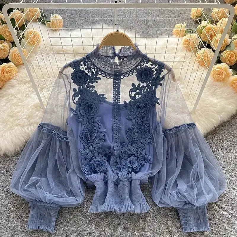 Blue lace puff long-sleeve blouse with sheer sleeves, floral embroidery, high neck and elastic cuffs.