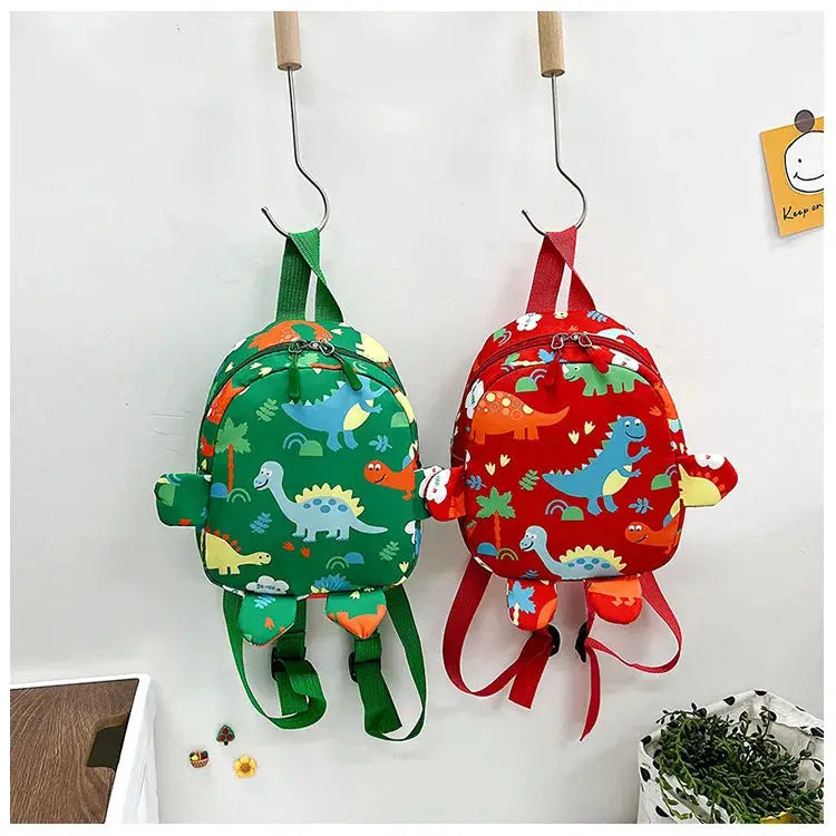 Two dinosaur kids backpacks by Simples Market, green and red cartoon dinos, anti-lost design
