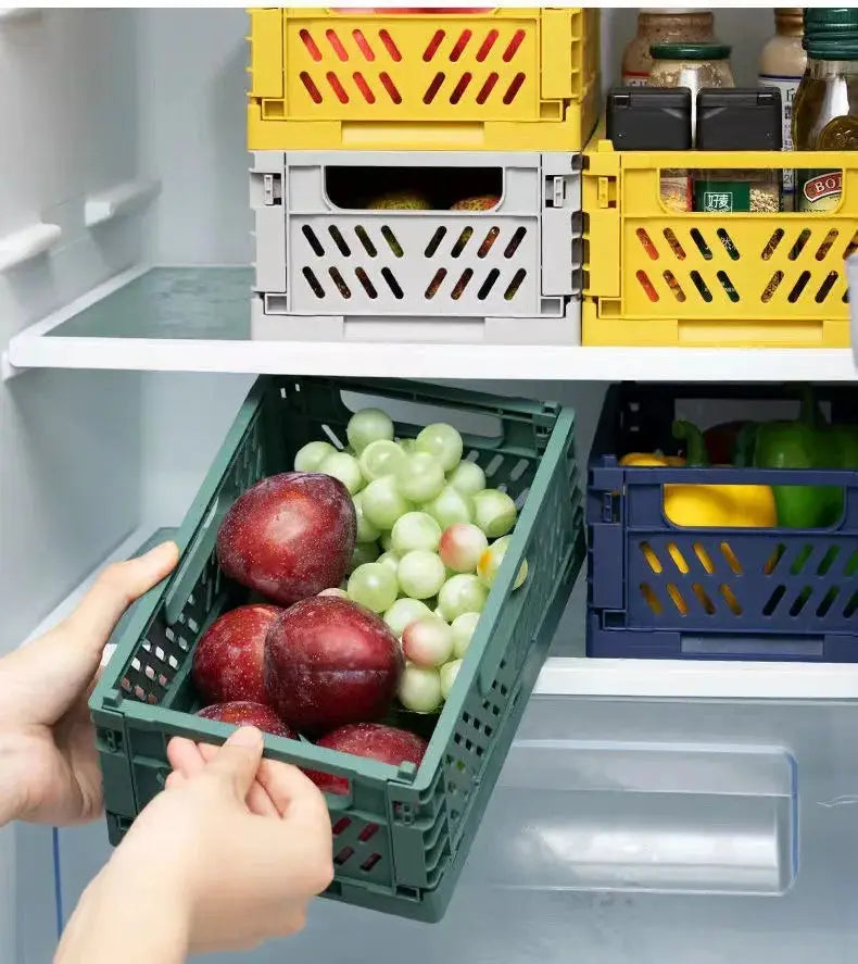 Plastic foldable storage crate by Simples Market; green foreground crate holding apples and grapes in a fridge with yellow and blue crates nearby