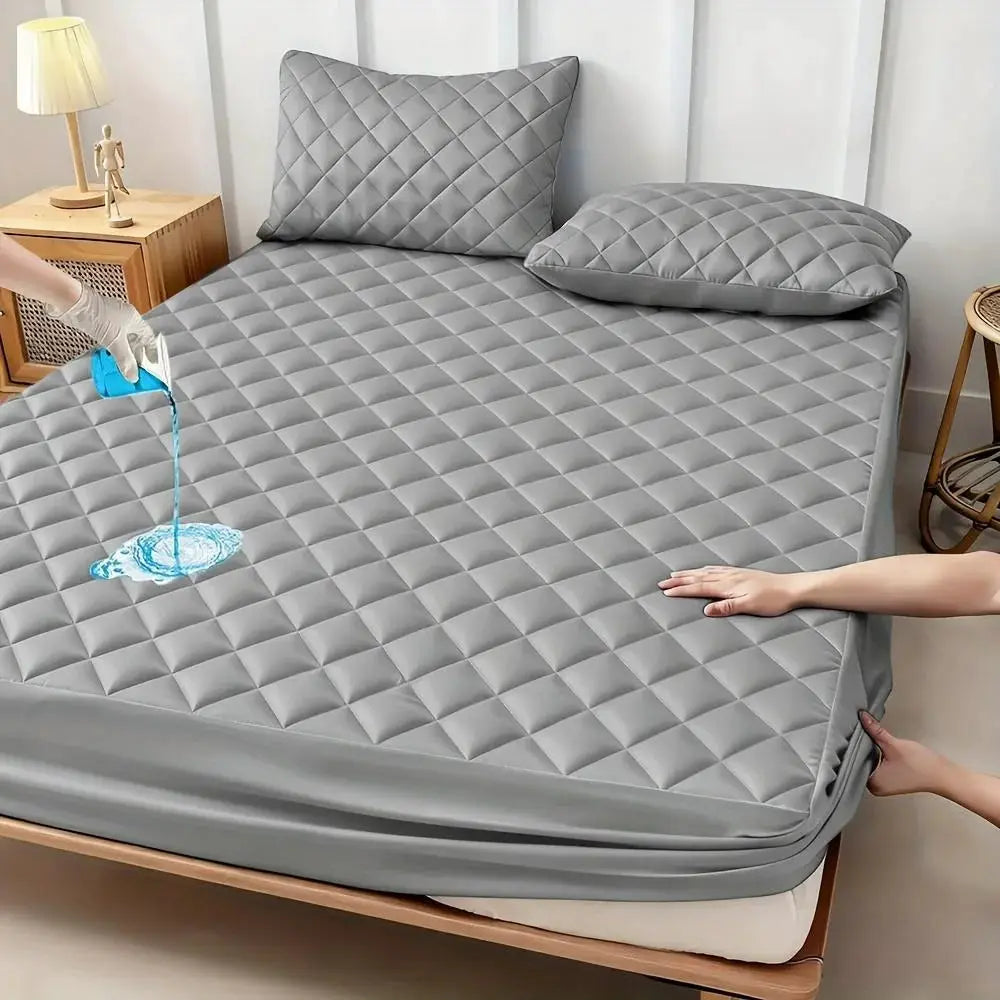 Mattress protector, gray quilted waterproof, on bed with two pillows.