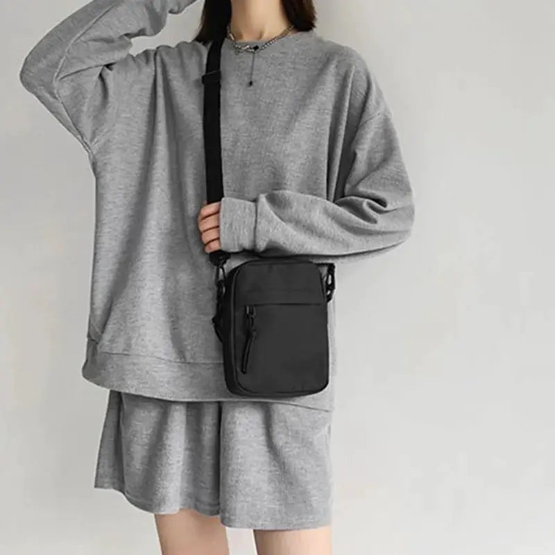 Crossbody bag, black compact single-shoulder design with front zipper pocket, worn with gray loungewear.