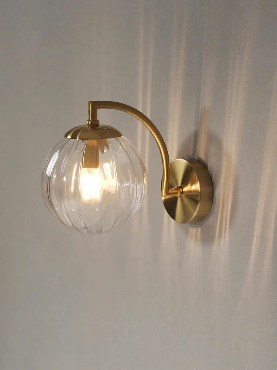 Modern LED wall lamp with brass curved arm and clear ribbed glass globe.