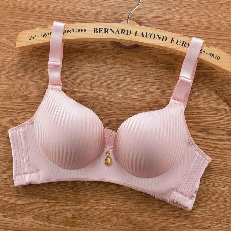 Padded pink wire-free bra with adjustable straps and center pendant, on a wooden hanger.