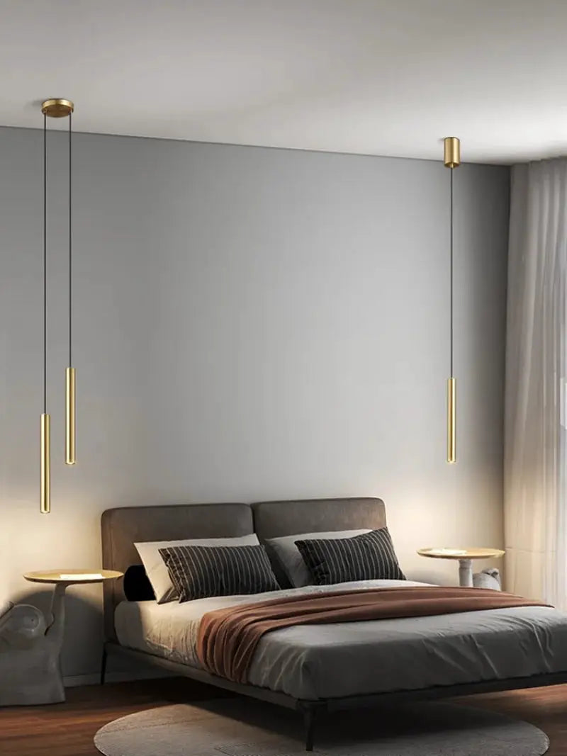 Minimalist gold bedside pendant lamps hanging over a gray upholstered bed with round nightstands