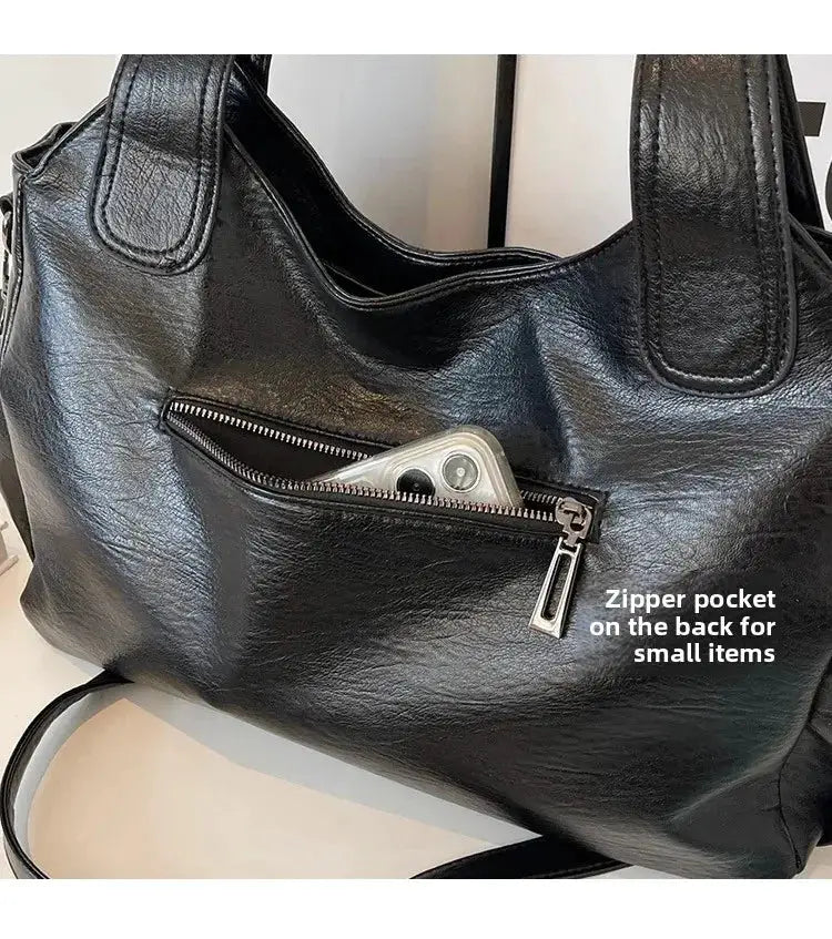 Black leather shoulder bag with back zipper pocket holding a smartphone.