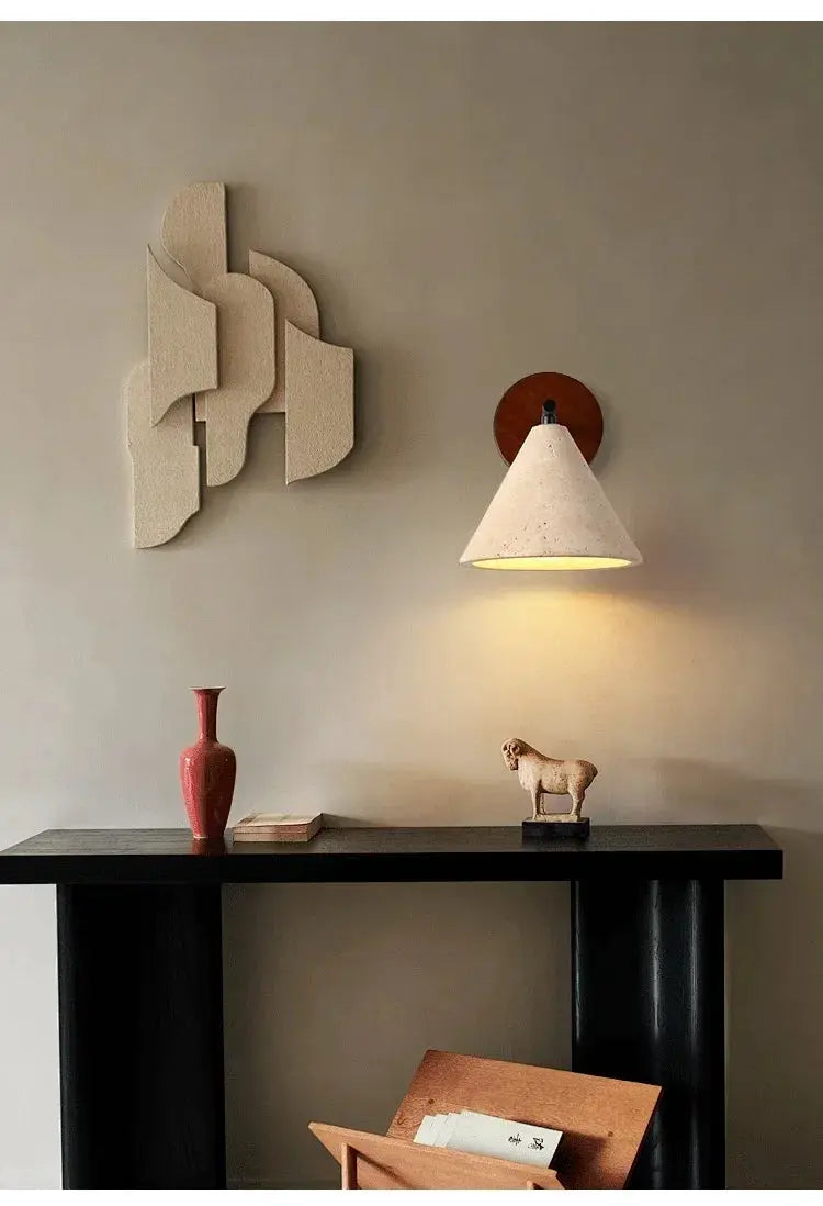 Natural stone travertine wall lamp sconce with conical shade and warm yellow light on brown mount beside wall art.