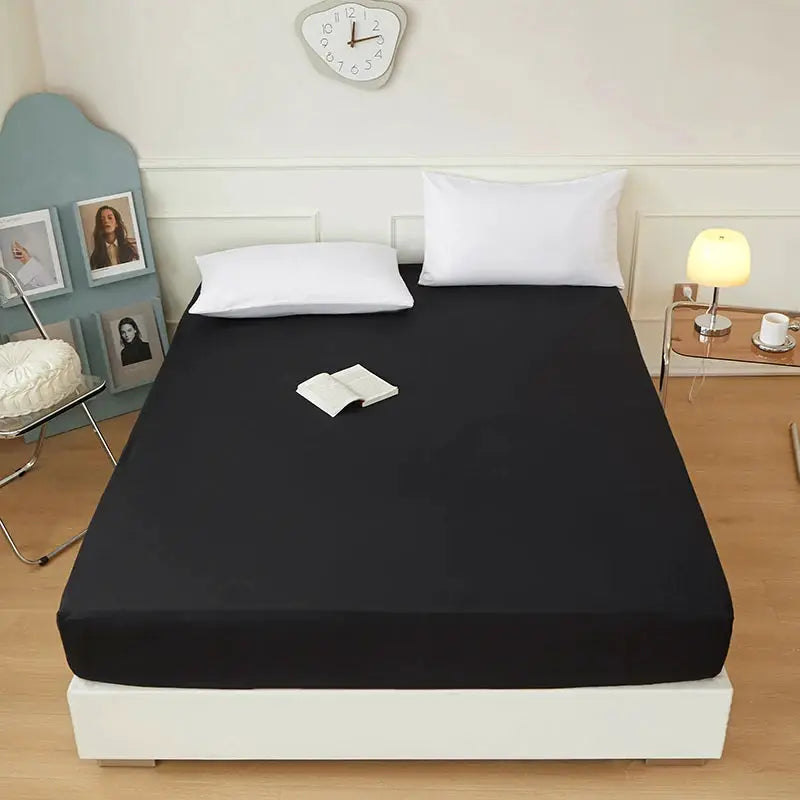Black polyester fitted bed sheet with elastic edges on a white bed in a tidy bedroom.