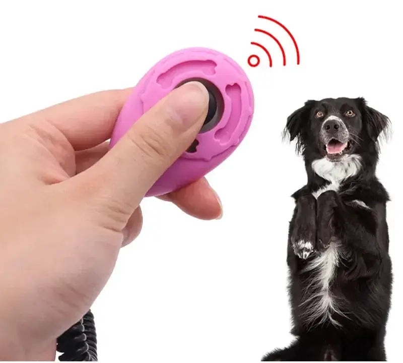 Adjustable dog training clicker by Simples Market - pink with wrist strap, shown beside a black-and-white dog