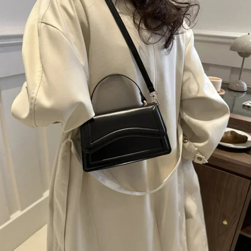 PU leather handbag, small black crossbody bag with top handle and white stitching.