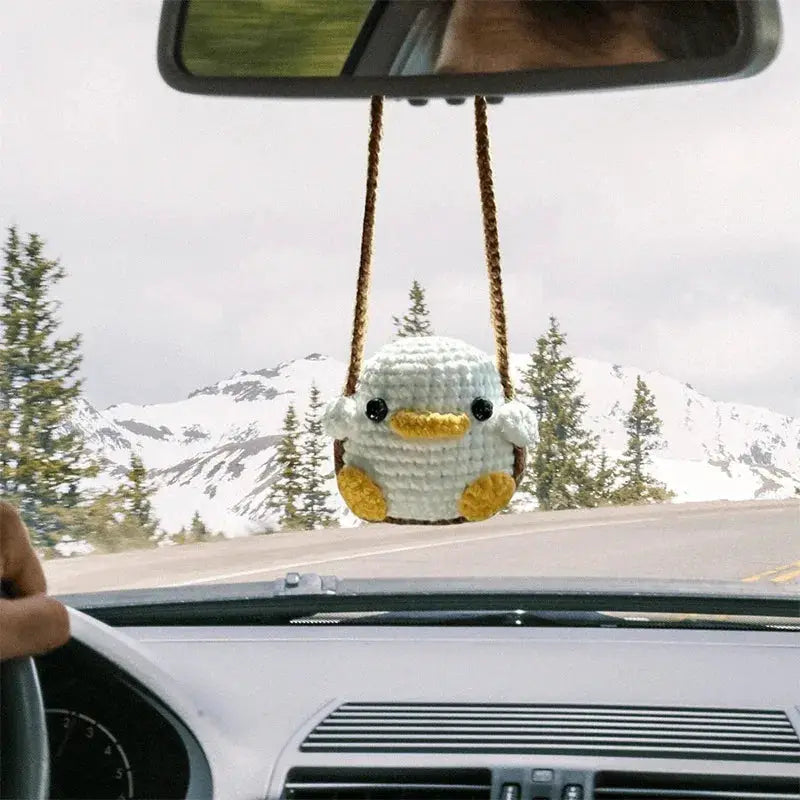 Crochet duck car pendant hanging from rearview mirror; white body with yellow beak and feet, brown cord.