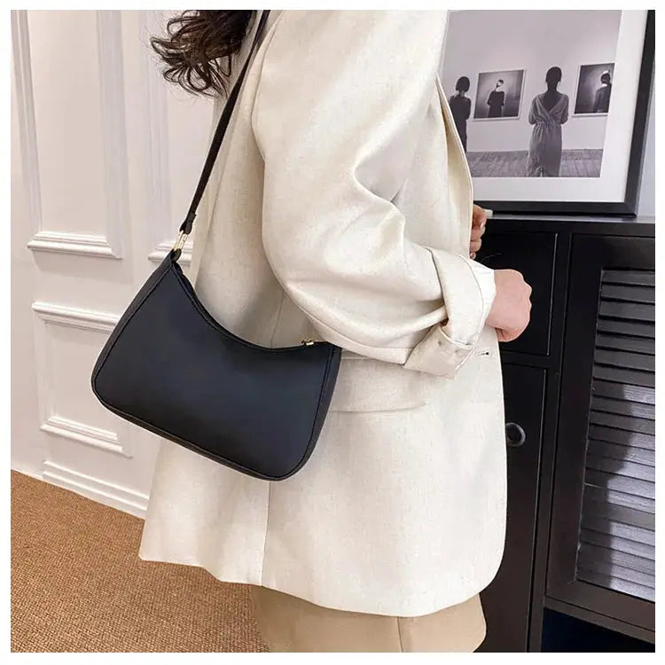 Handbag, small black square with shoulder strap worn over a beige coat.