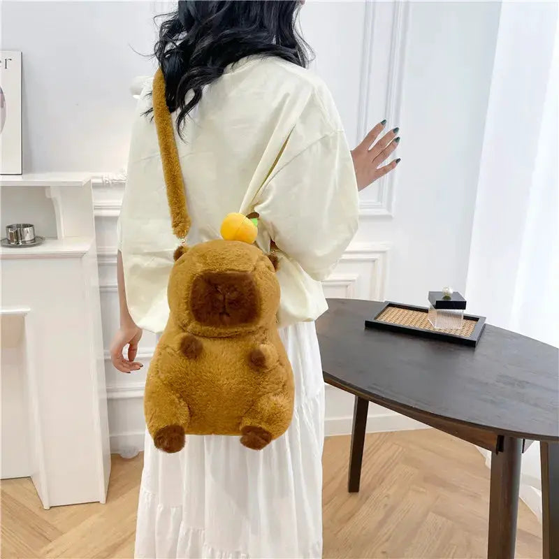Capybara plush backpack in brown with carrot charm, worn crossbody by a woman in white dress