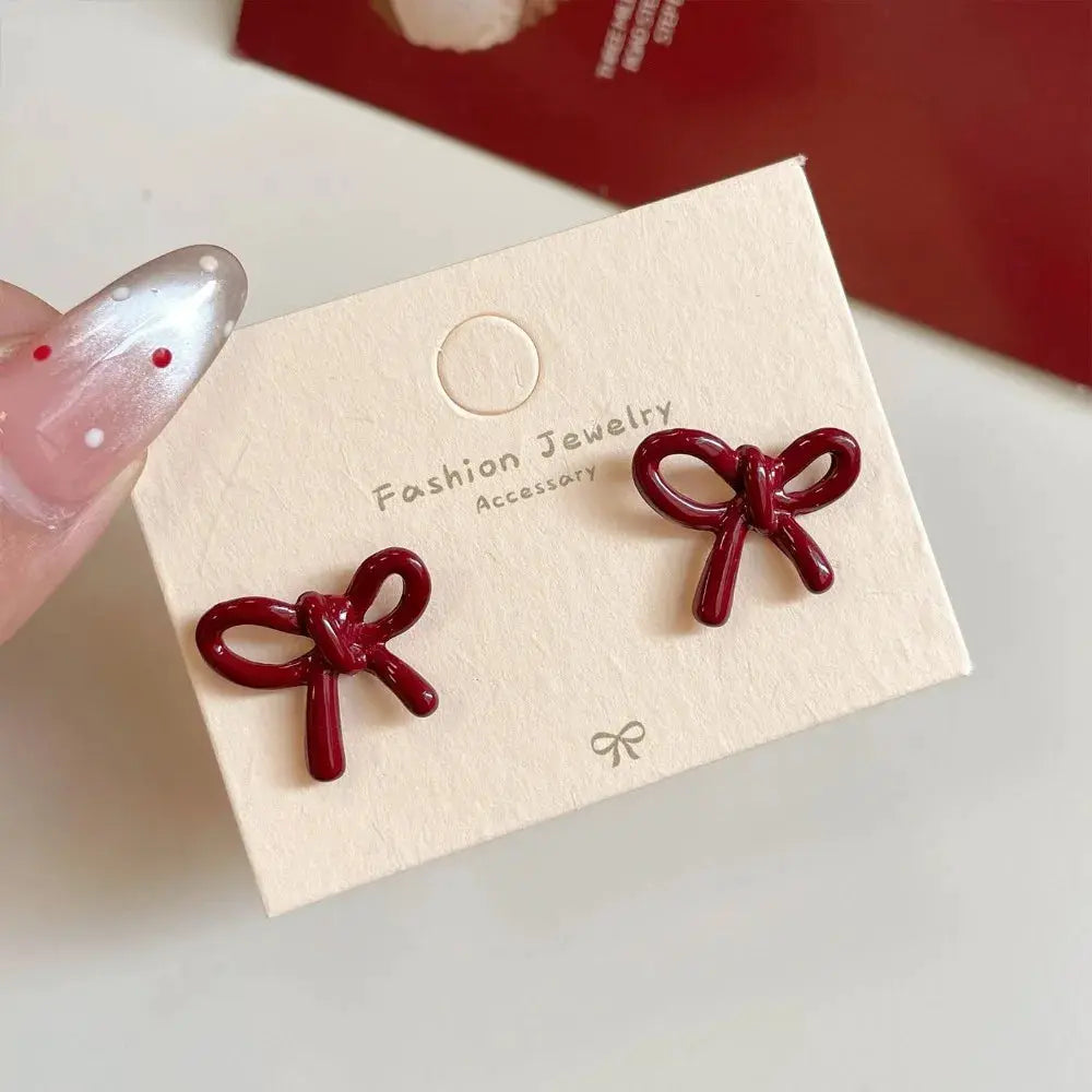 Red bowknot stud earrings pair in burgundy enamel on a beige display card