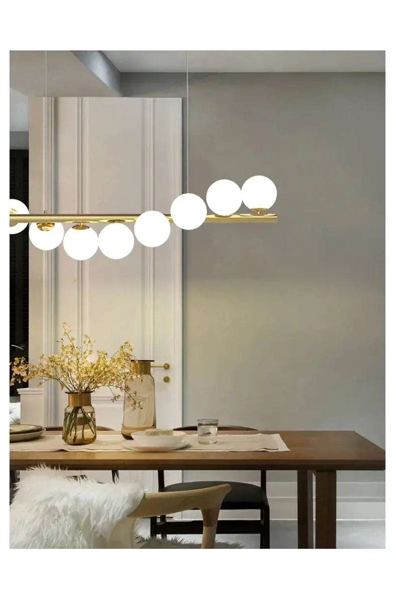 Nordic ceiling chandelier with a gold bar and white globe bulbs above a wooden dining table