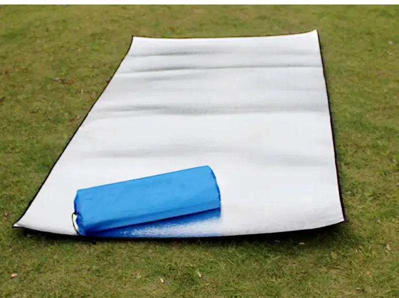 White aluminum-insulated camping foam mat with blue rolled carry bag on grass