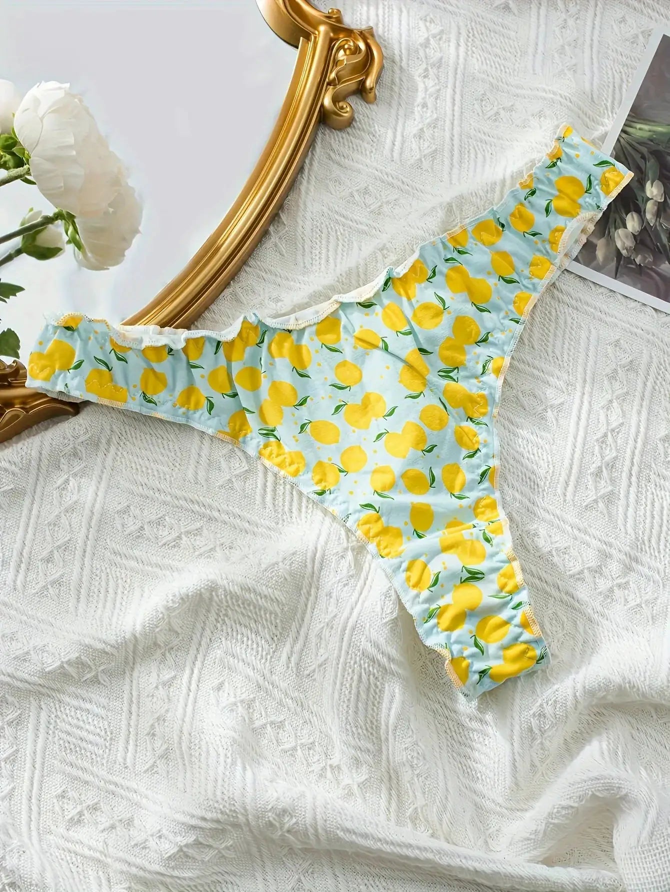 Cotton lemon-print thong on light blue background with yellow lemons and ruffled trim.