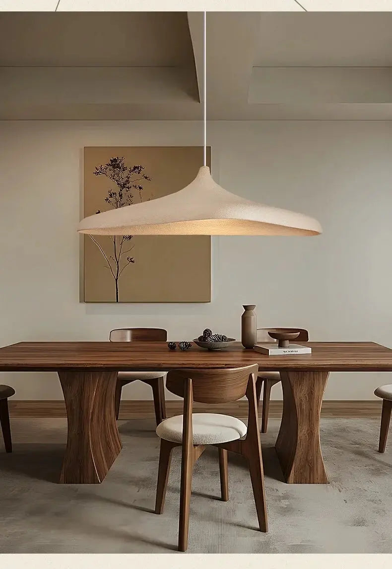 One cream-colored LED pendant light in Japanese wabi-sabi style hanging over a wooden dining table.