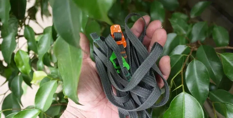 Luggage strap in grey nylon, tangled, with orange quick-release buckle held in hand.