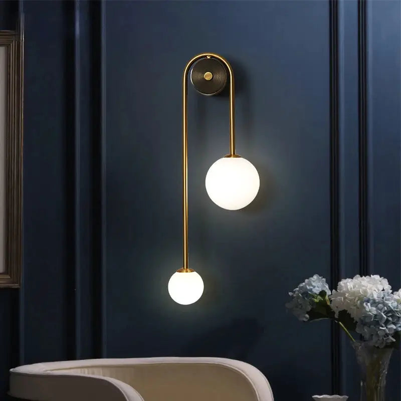 Wall lamp by Simples Market with a gold metal frame and two glass globe LED bulbs.
