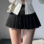 Pleated black mini skirt with an A-line silhouette, paired with a white button-down top and beige handbag.