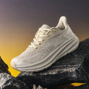 Men's running shoes in cream mesh with cushioned sole and breathable upper, rugged outdoor trainer on rocky surface