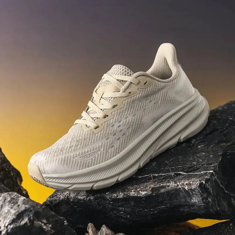 Men's running shoes in cream mesh with cushioned sole and breathable upper, rugged outdoor trainer on rocky surface