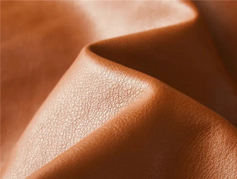 Leather jacket fabric close-up in brown tones, highlighting rich leather grain and soft folds