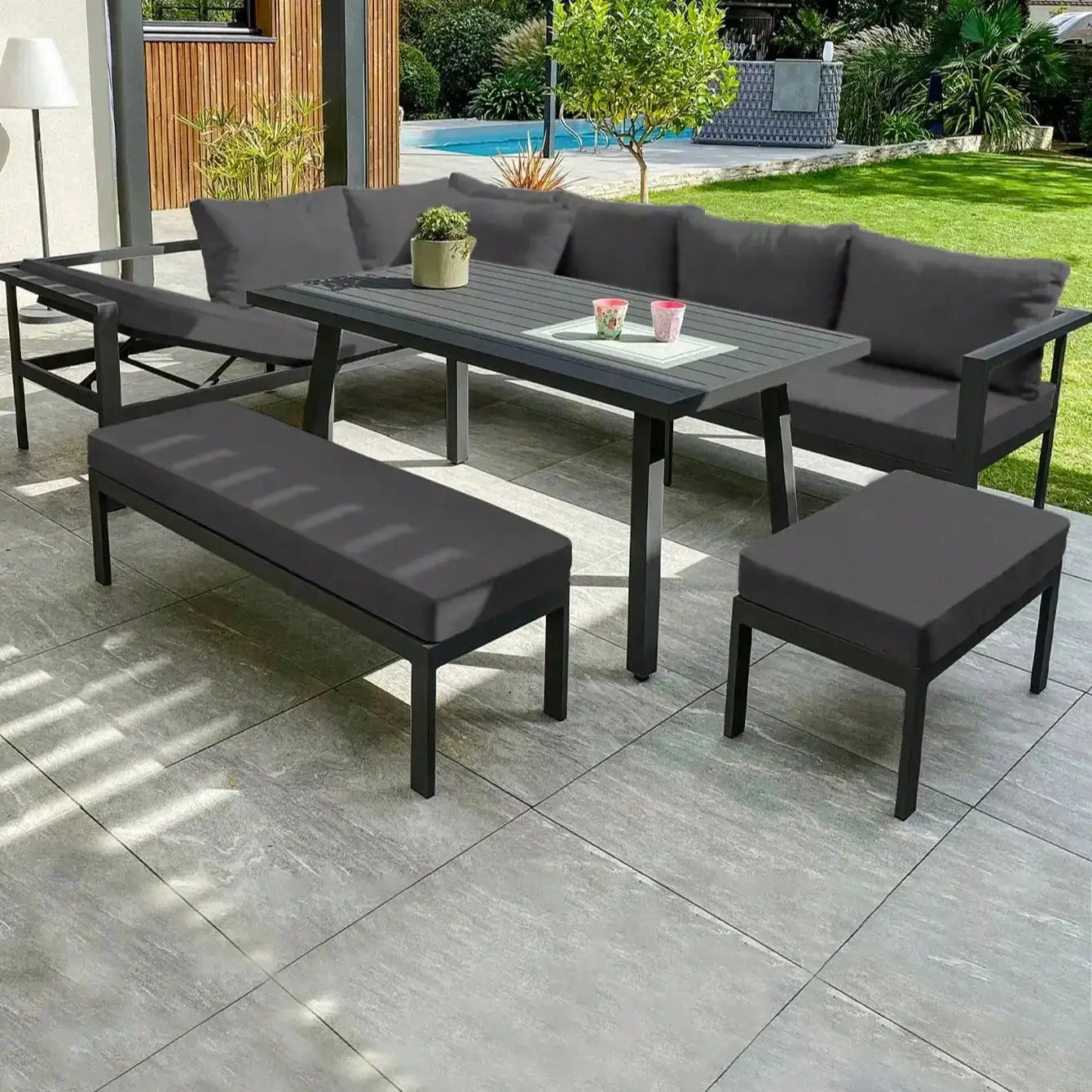 Outdoor patio furniture cushions in dark gray on a sofa set with bench and ottomans around a rectangular table.