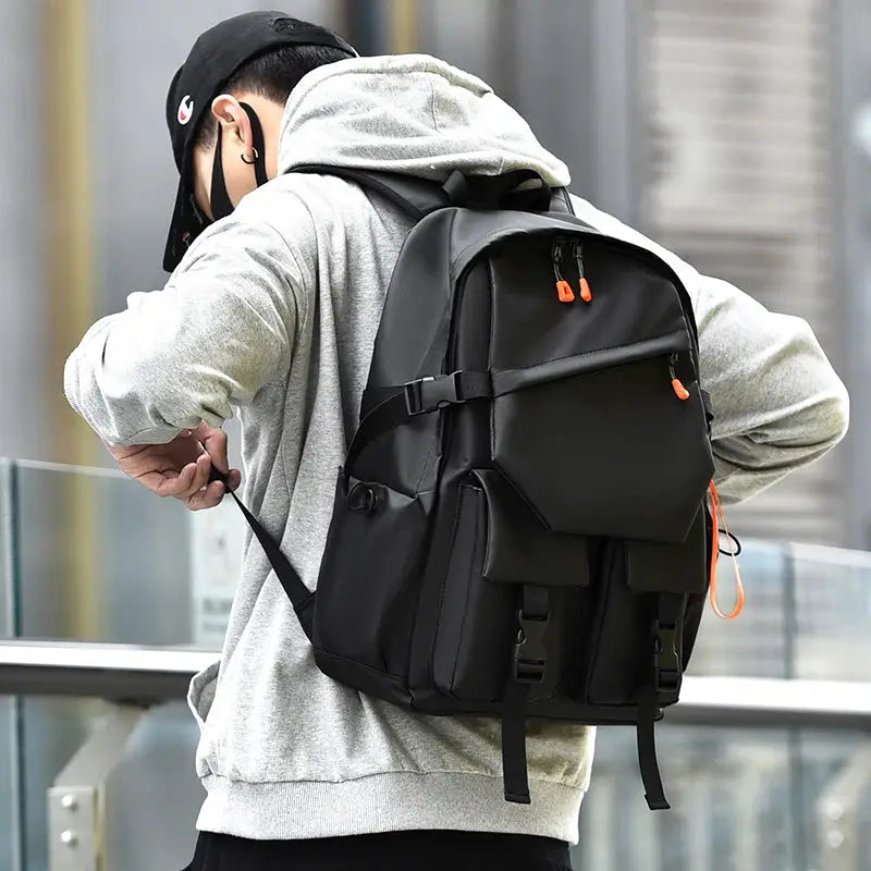 Luxury men's backpack in black with orange zipper pulls and multiple pockets, worn by a man in a gray hoodie.