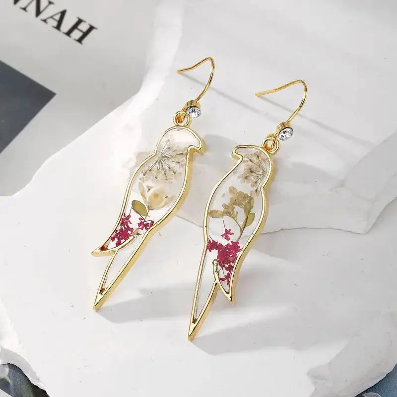 Gold-tone pressed-flower epoxy resin dangle earrings with clear floral interior and pink-red accents, pair
