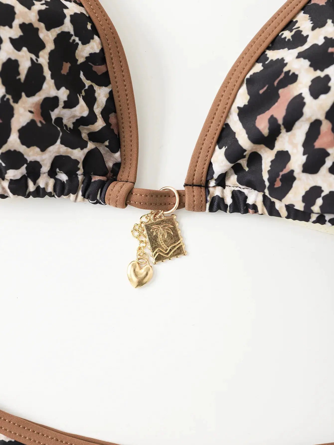 Triangle bikini top in leopard print with tan straps and gold charms (heart and palm-tree pendants) at center.