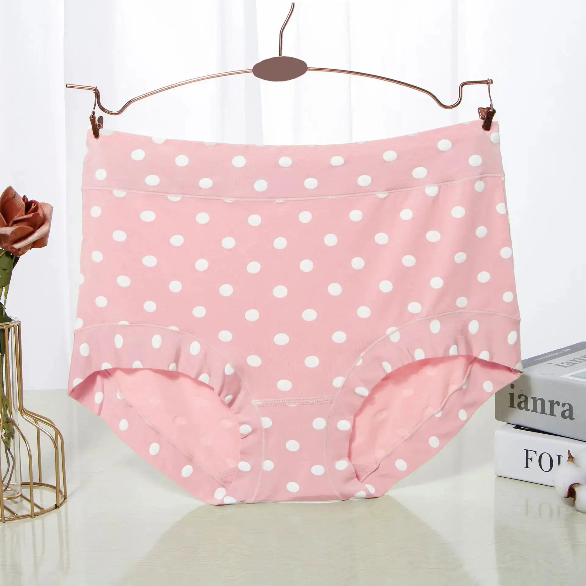 Pink polka-dot high-waist panties hanging on a copper hanger against a white background