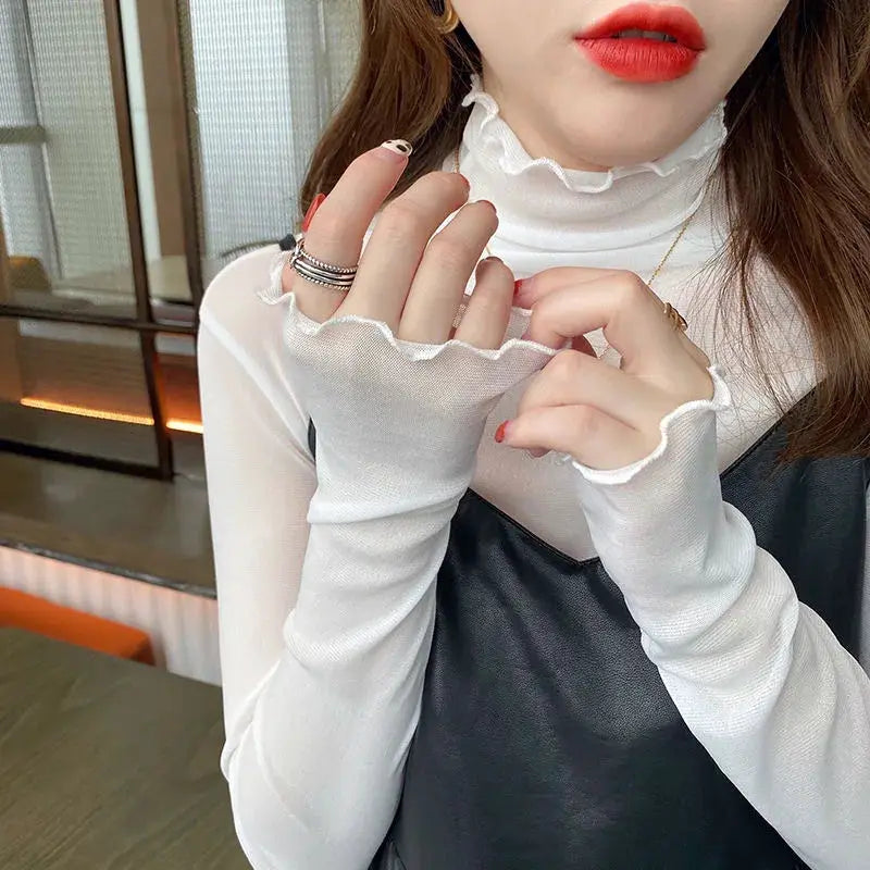 White sheer mesh blouse with a ruffled high-neck and cuffs, worn over a black slip dress.