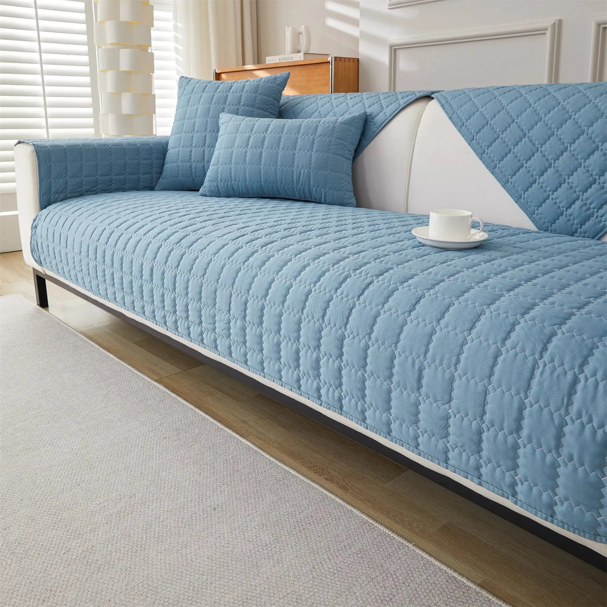 Sofa cover with blue quilted anti-slip fabric and 2 matching cushions on a white sofa