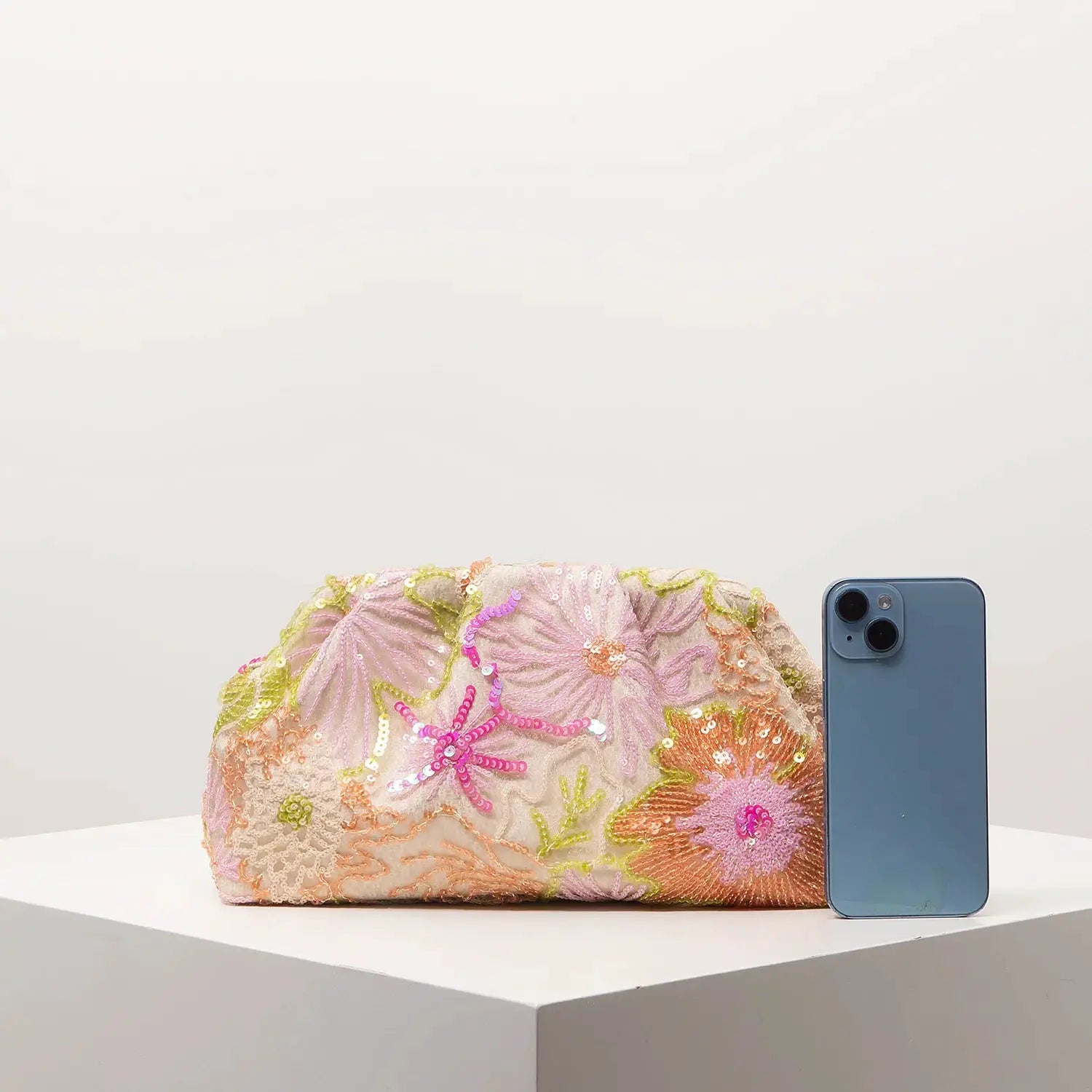 Sequin floral clutch bag with pastel embroidery beside a blue iPhone