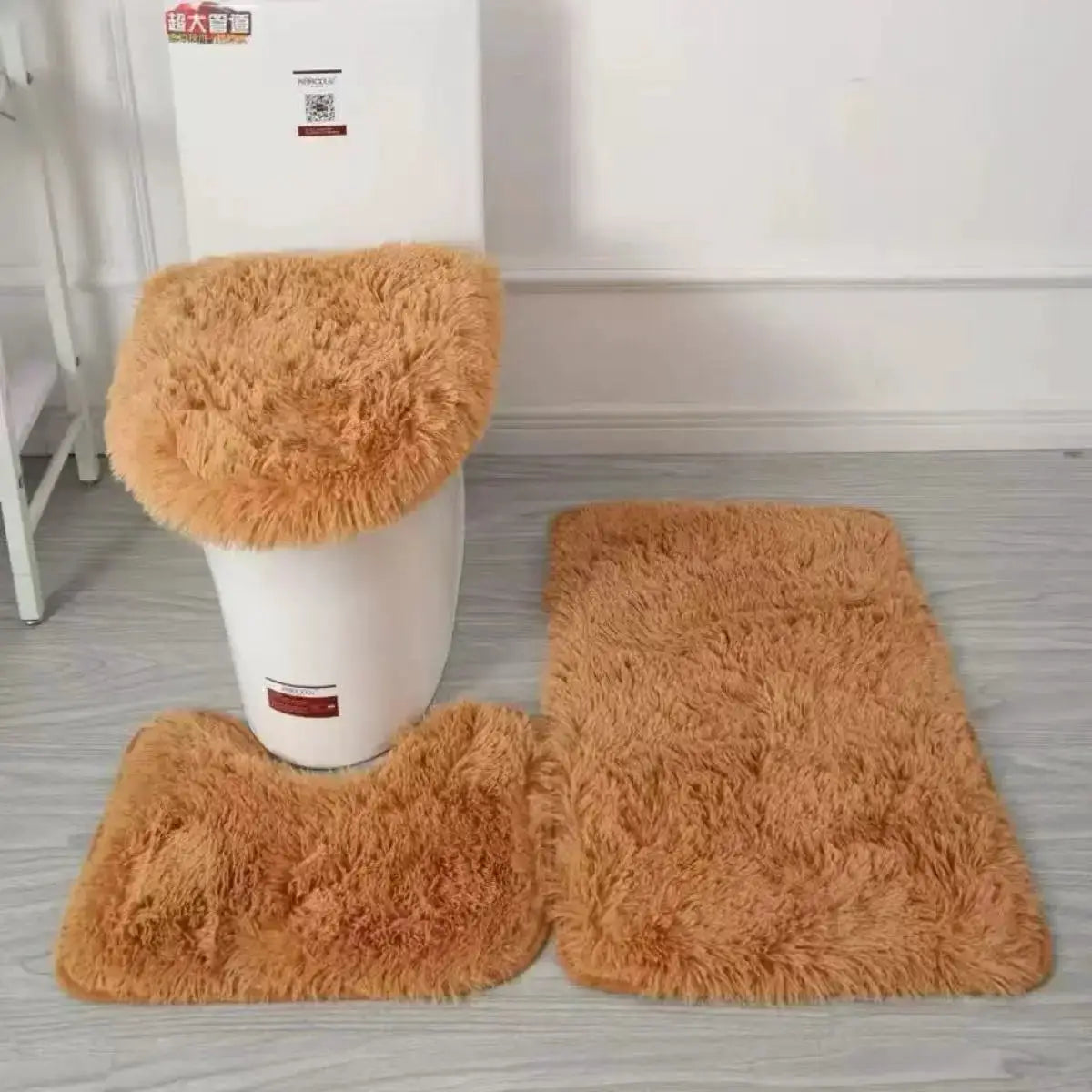 3-piece tan plush bathroom rug set: toilet lid cover, U-shaped rug, and rectangular bath mat.